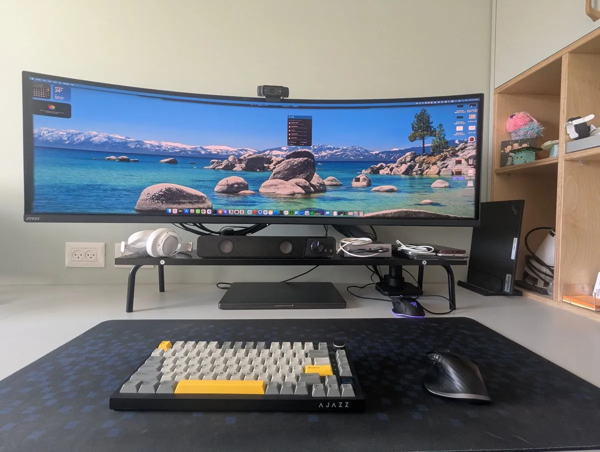The desk head-on: a 49 inch curved MSI ultrawide on a riser, AJAZZ mechanical keyboard, MX Master mouse, soundbar, and headphones